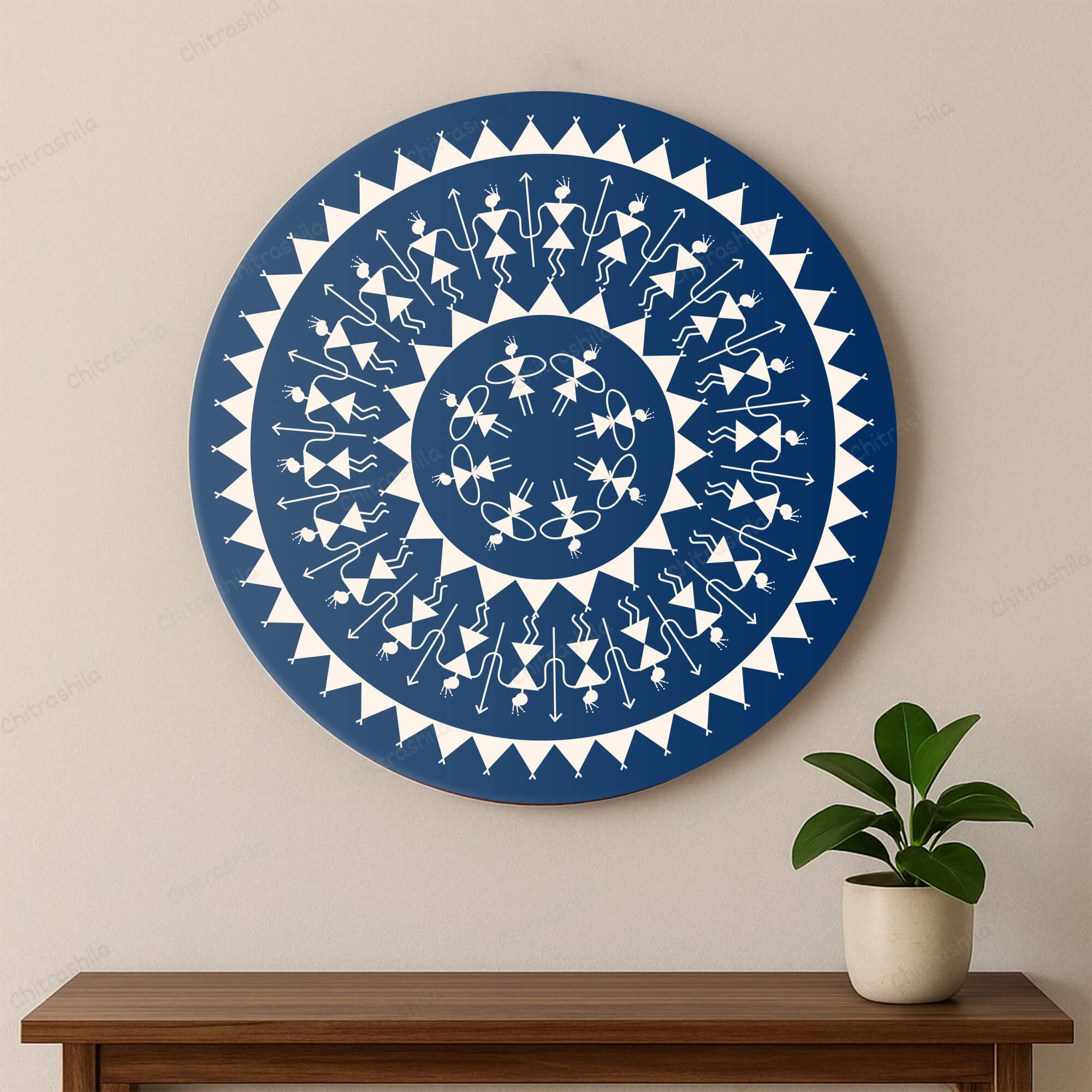 Decorative blue and white circular Warli wall art on a beige wall with a wooden bench and plant below.
