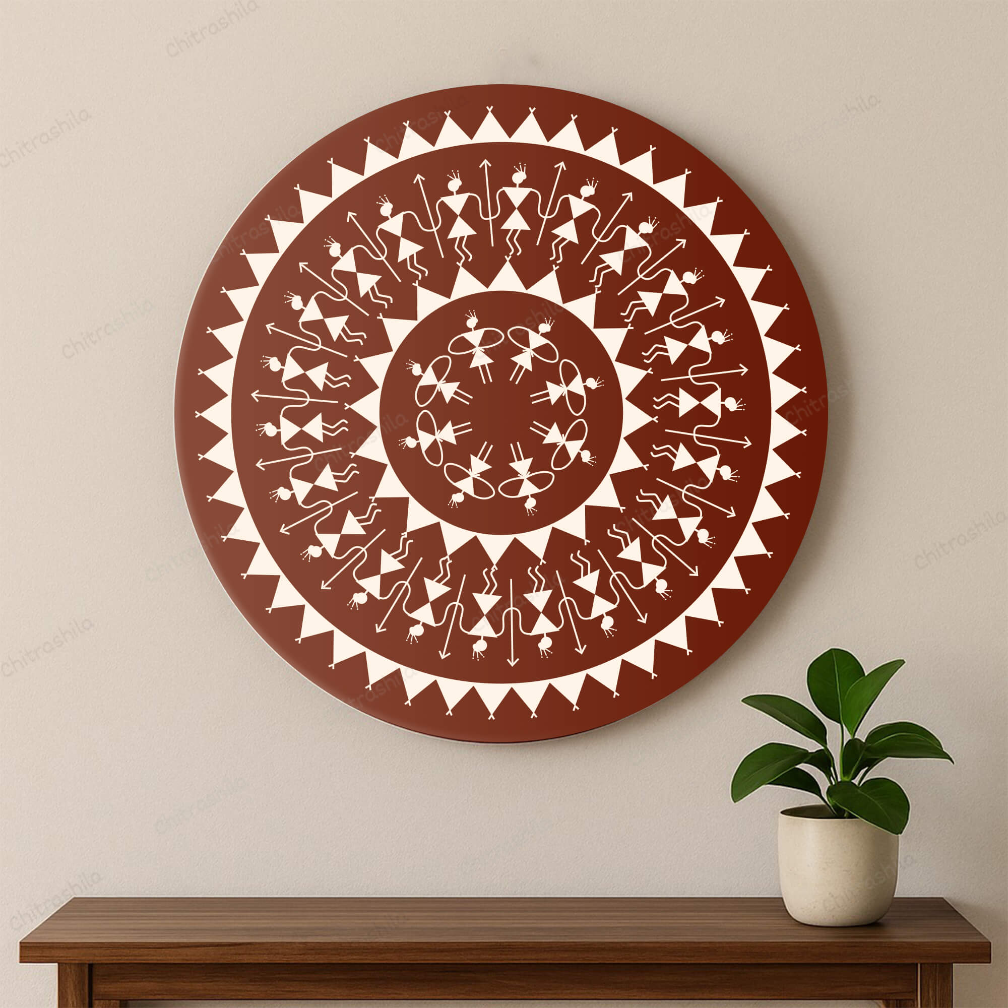 Decorative circular wall art with Warli patterns on a beige wall, below a wooden shelf with a plant.